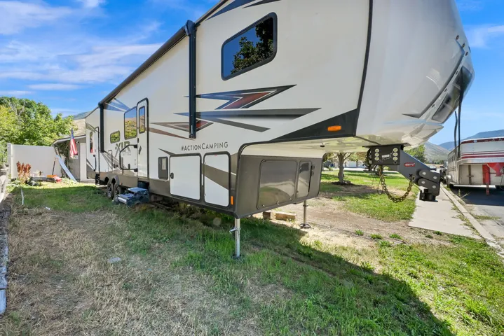 RV exterior featuring a prominent awning, multiple windows, integrated storage compartments, and a fifth-wheel hitch