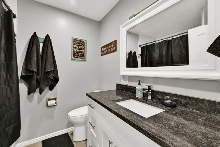 White vanity with dark stone countertop, integrated rectangular sink, and chrome faucet