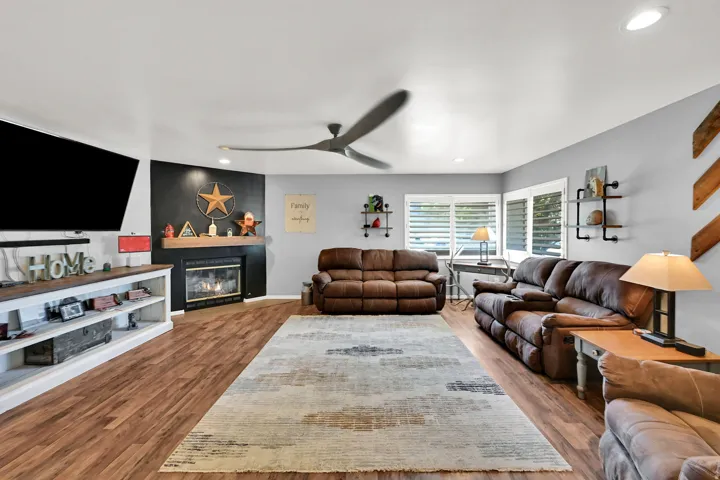 Living area with wood-finish flooring, a corner fireplace, and a ceiling fan