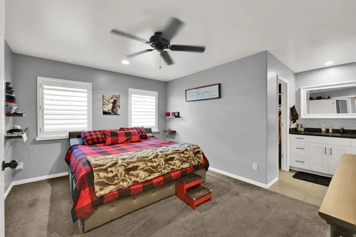 Carpeted room with a ceiling fan, two windows with white blinds, and built-in shelving