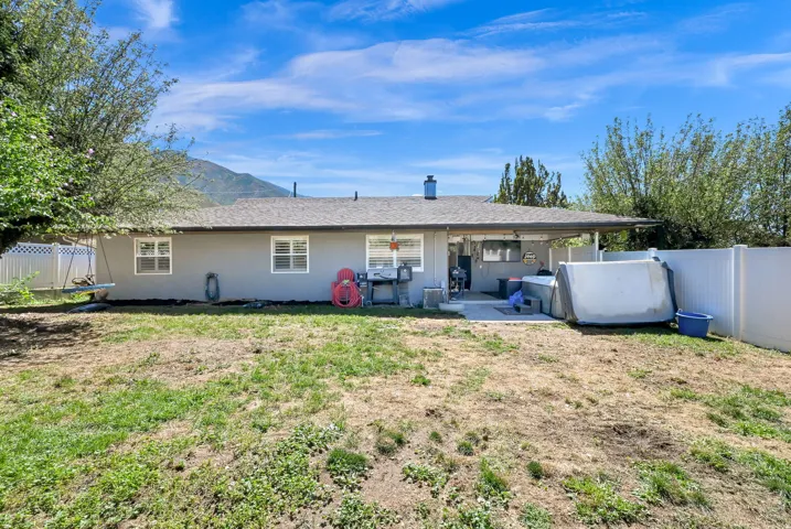 Expansive backyard featuring a covered patio, white fencing, and a mountain backdrop