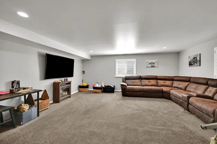 Spacious living area featuring neutral carpeting, recessed ceiling lighting, and a window with white shutters