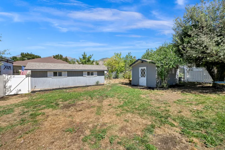 Expansive yard with two storage sheds, a white privacy fence, and mature trees
