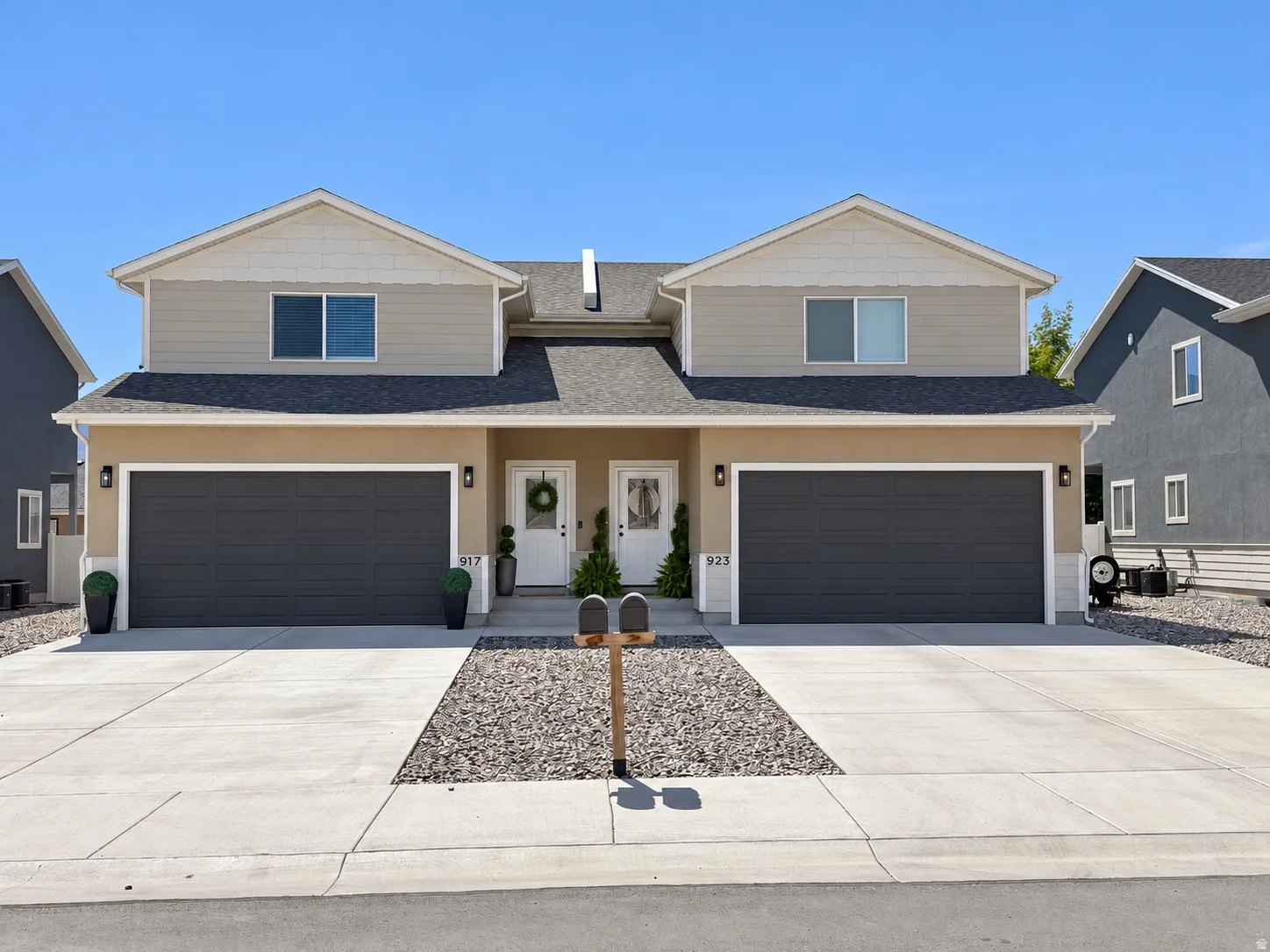 Duplex exterior featuring two single-car garages, a pitched shingle roof, and a gravel and concrete driveway