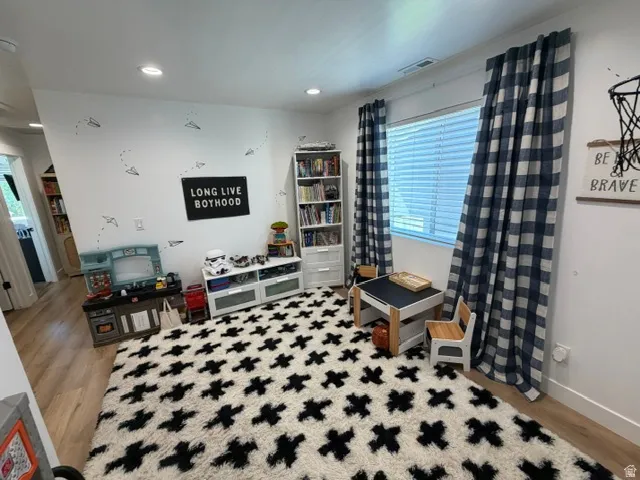 Recessed lighting illuminates the wood-finish flooring in this versatile room, featuring a window with blinds and full-length plaid drapes