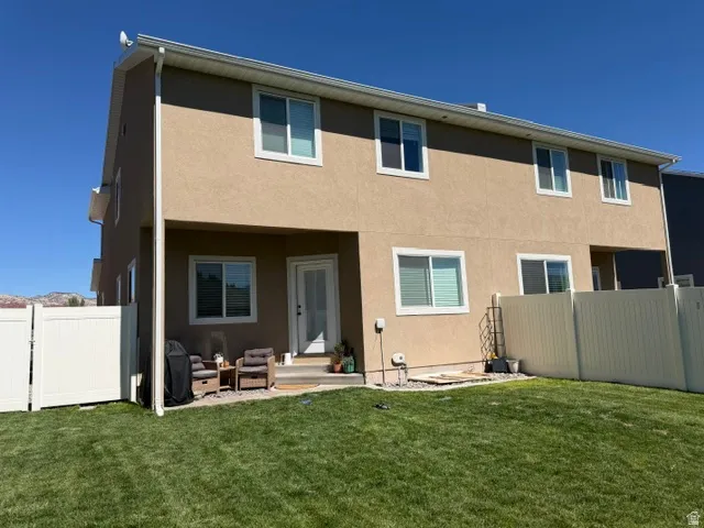 Expansive backyard featuring a manicured lawn, full vinyl fencing, and a stucco exterior with multiple windows