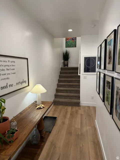 Wood-finish flooring with white baseboards, carpeted staircase, and recessed ceiling lighting