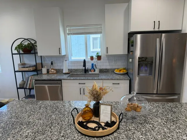 Kitchen featuring granite countertops, white cabinetry with black hardware, subway tile backsplash, stainless steel appliances, and a stainless steel sink with a black pull-down faucet