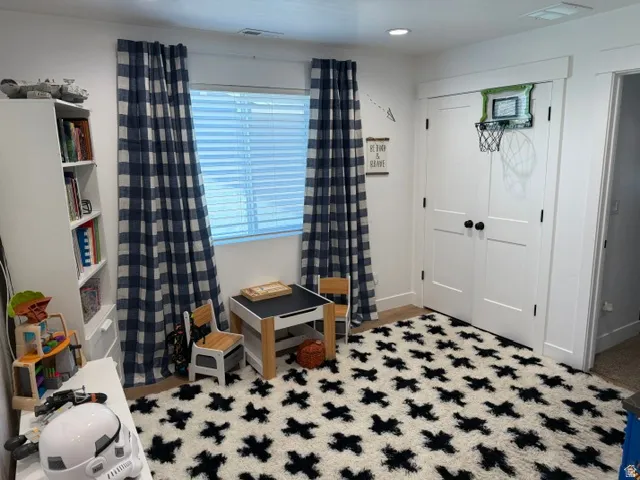 White walls with a window featuring blinds, wood-finish flooring, and a built-in shelving unit