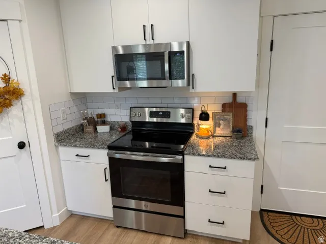 White cabinetry with matte black hardware, stainless steel appliances, granite countertops, and subway tile backsplash