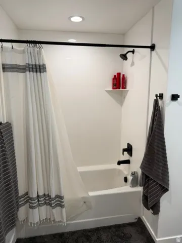 White bathtub with integrated shower, matte black fixtures, and a corner storage shelf