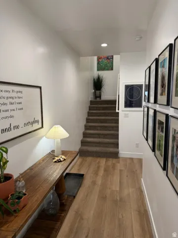 Wood-finish flooring with white baseboards, carpeted staircase, and recessed ceiling lighting