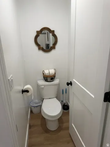 White interior walls and trim, wood-finish flooring, and a white two-piece toilet