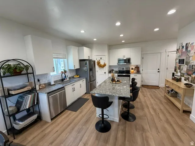 Kitchen with wood-finish flooring, white cabinetry, stainless steel appliances, and recessed lighting