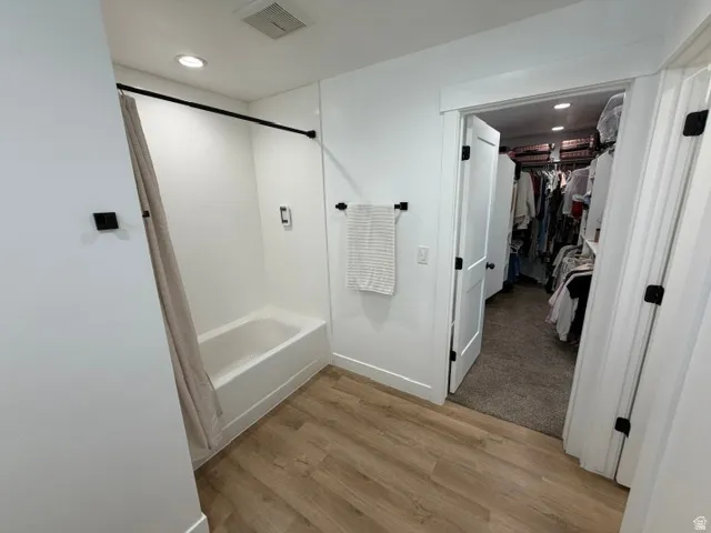 Bathroom featuring wood-finish flooring, a white bathtub with integrated shower, and recessed ceiling lighting