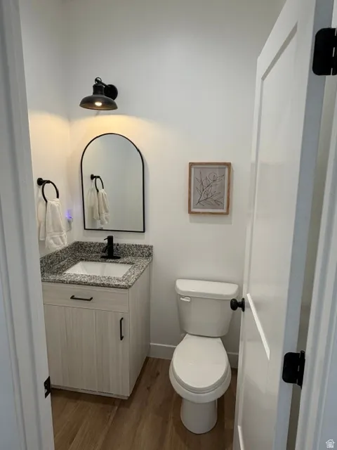 Bathroom featuring a light-toned wood-finish vanity, speckled countertop, black-finish faucet, and wood-finish flooring