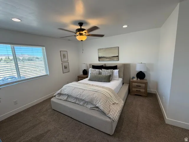 Recessed lighting, ceiling fan with integrated light, large window with horizontal blinds, built-in bedside tables with drawer storage, and carpeted flooring