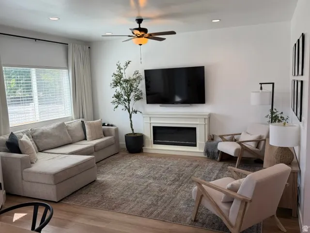 Recessed lighting, wood-finish flooring, electric fireplace with mantel, ceiling fan with integrated lighting, and window blinds
