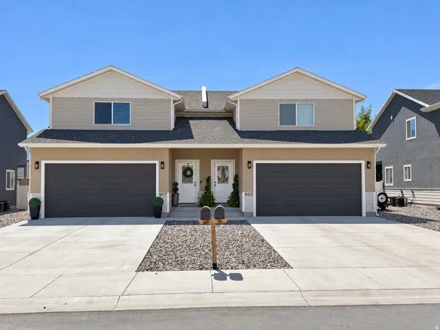 Duplex exterior featuring two single-car garages, a pitched shingle roof, and a gravel and concrete driveway