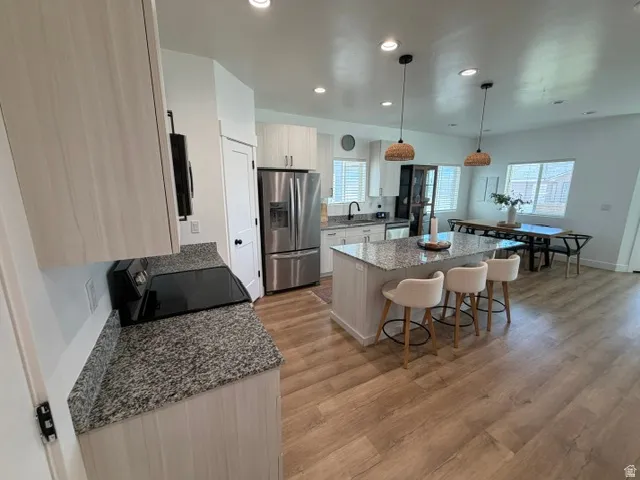 Kitchen featuring wood-finish flooring, light-toned cabinetry, speckled countertops, stainless steel appliances, and an island with pendant lighting