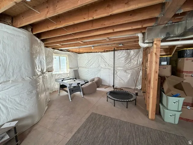 Basement space featuring exposed wood joists, a finished concrete floor, and an egress window