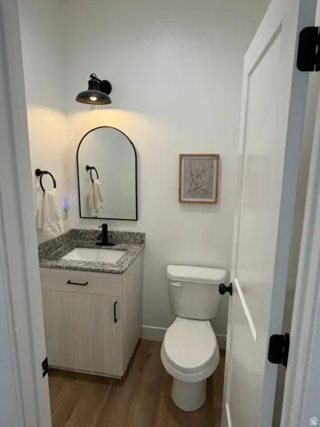 Bathroom featuring a light-toned wood-finish vanity, speckled countertop, black-finish faucet, and wood-finish flooring