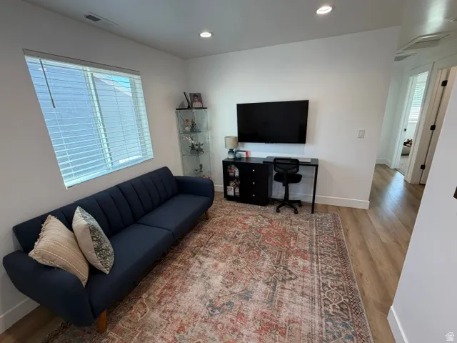 Recessed lighting, light wood-finish flooring, white wall finishes, and a large window with blinds