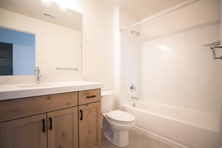Full secondary bath with stained wood cabinets and quartz slab countertops.
