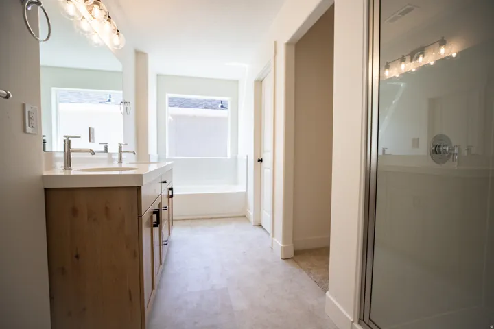 Primary bath with dual sinks, stained wood cabinets, quartz slab countertops, soaker tub and walk-in shower.