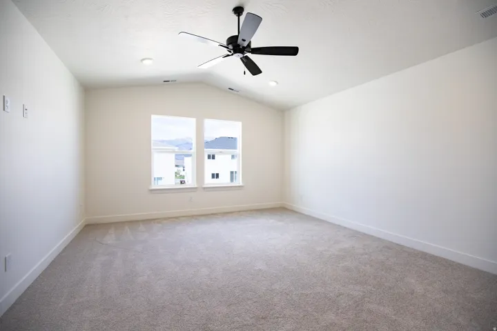 Primary bedroom with vaulted ceiling and ceiling fan.