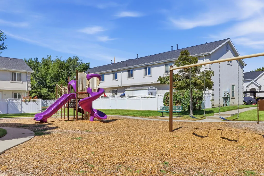 Outdoor play area featuring a multi-level play structure with slides, a swing set, and a wood chip surface