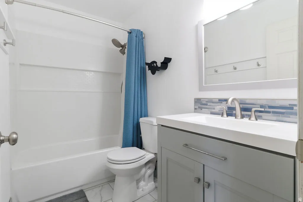 White bathtub with shower, toilet, and a vanity with a rectangular sink