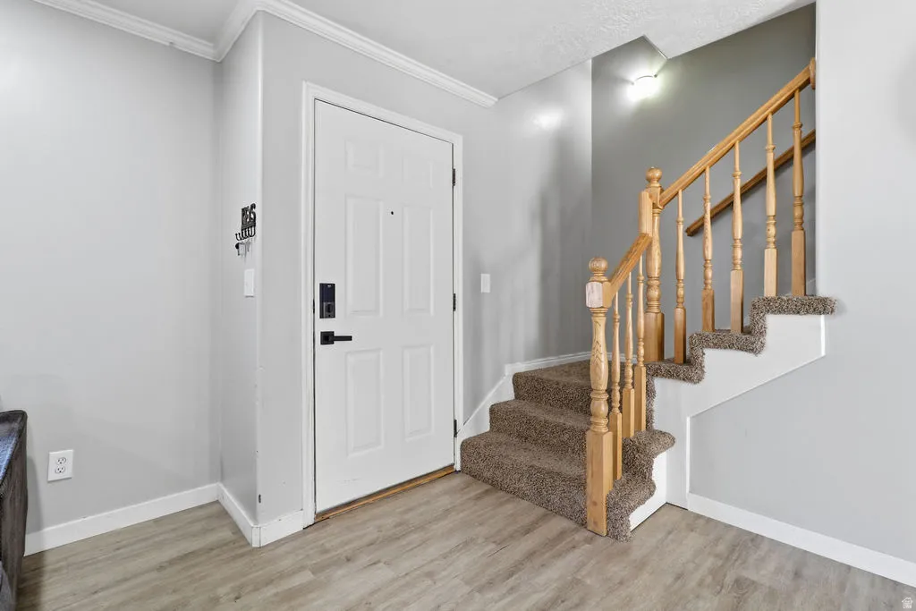 Entryway featuring a paneled door with black hardware, wood-finish flooring, and a carpeted staircase with a wood handrail and balusters