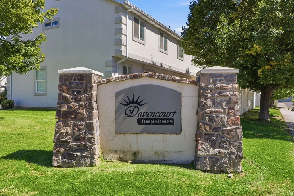 Stone-clad entry monument with a prominent community sign, surrounded by green grass and mature trees