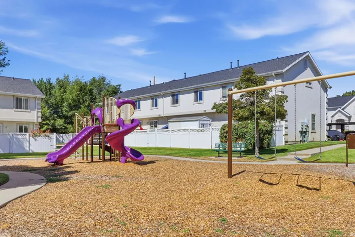 Outdoor play area featuring a multi-level play structure with slides, a swing set, and a wood chip surface