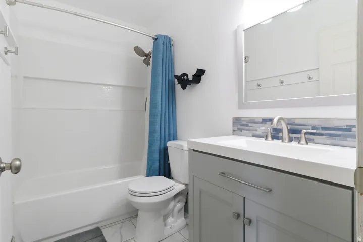 White bathtub with shower, toilet, and a vanity with a rectangular sink