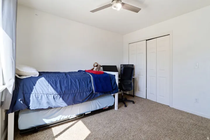 Neutral tone wall paint, carpet flooring, ceiling fan with integrated lighting, and bi-fold closet doors