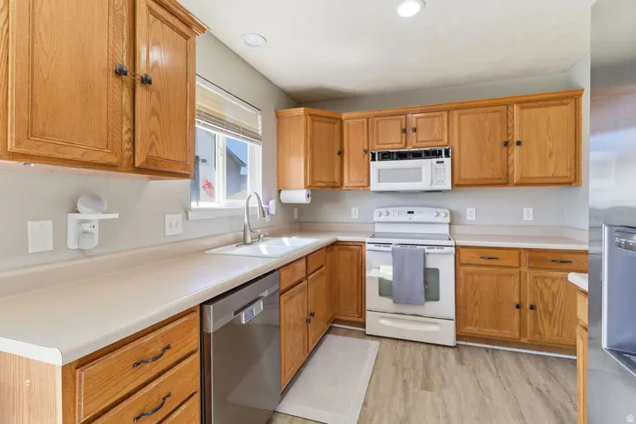 Kitchen with wood-finish cabinetry, solid surface countertops, a white built-in microwave, white range, and stainless steel dishwasher