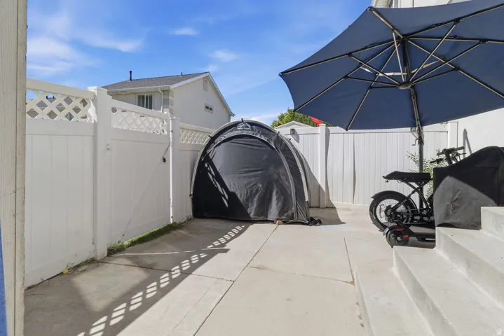 Concrete patio with steps, white privacy fencing with lattice accents, and a storage structure