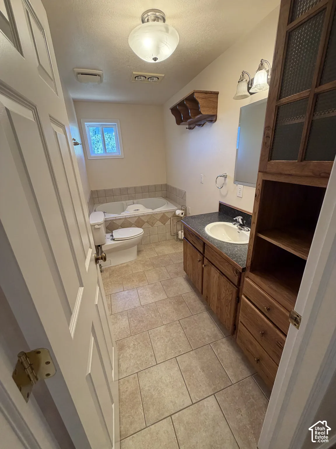 Tile flooring, deep soaking tub, single vanity, built-in storage cabinetry, and recessed lighting