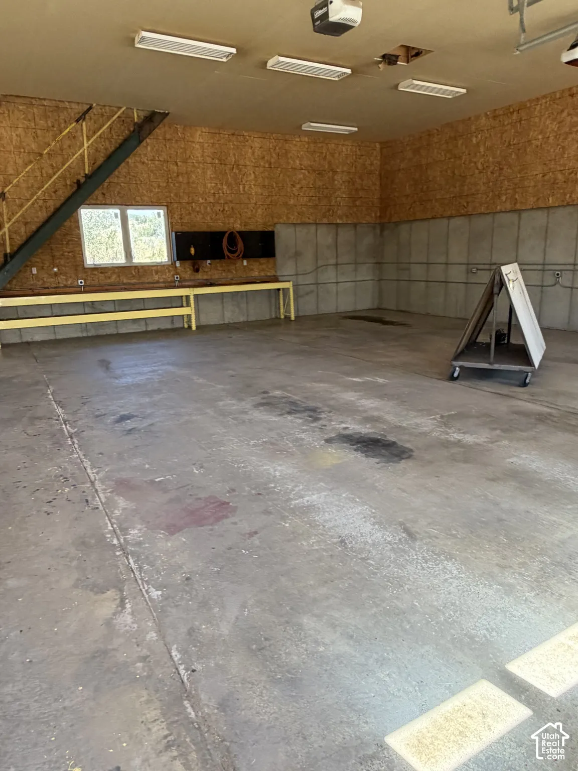 Concrete flooring with built-in workbench, wall-mounted electrical outlets, and overhead fluorescent lighting fixtures