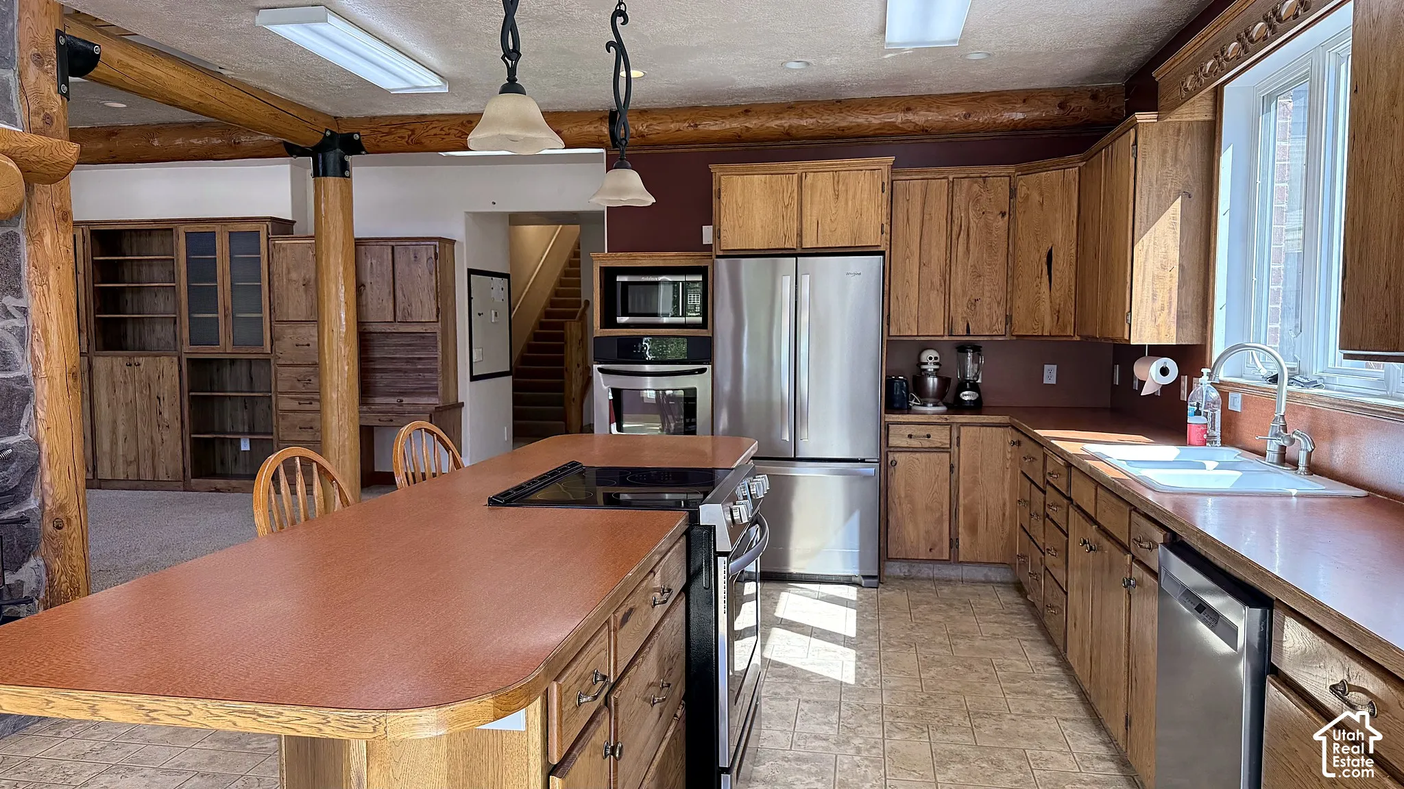 Kitchen featuring wood cabinetry, stainless steel appliances, a central island with an integrated cooktop, decorative log support beams, and built-in shelving
