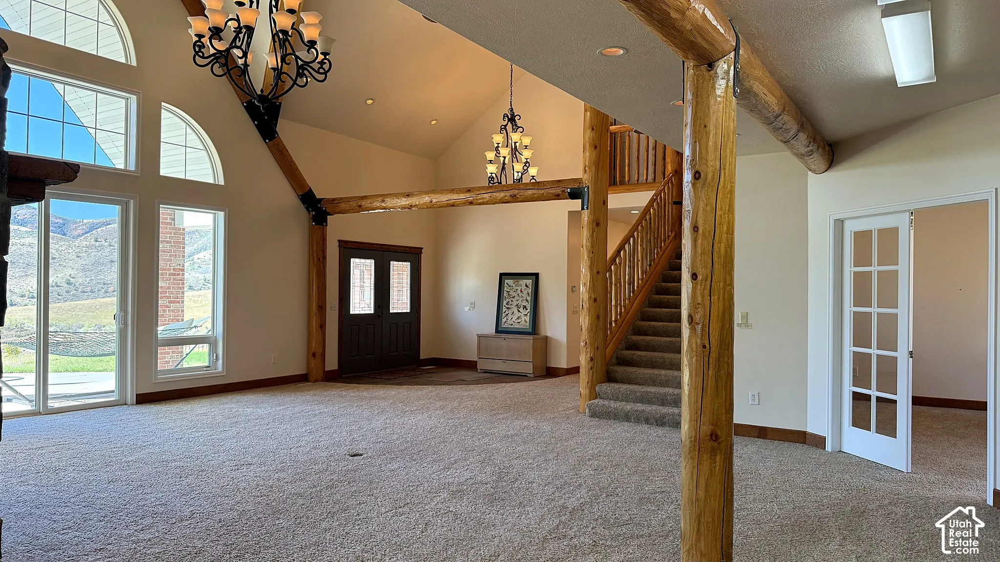Great room featuring vaulted ceilings, exposed log beams, arched windows, dual wrought-iron chandeliers, and a staircase with a wooden railing
