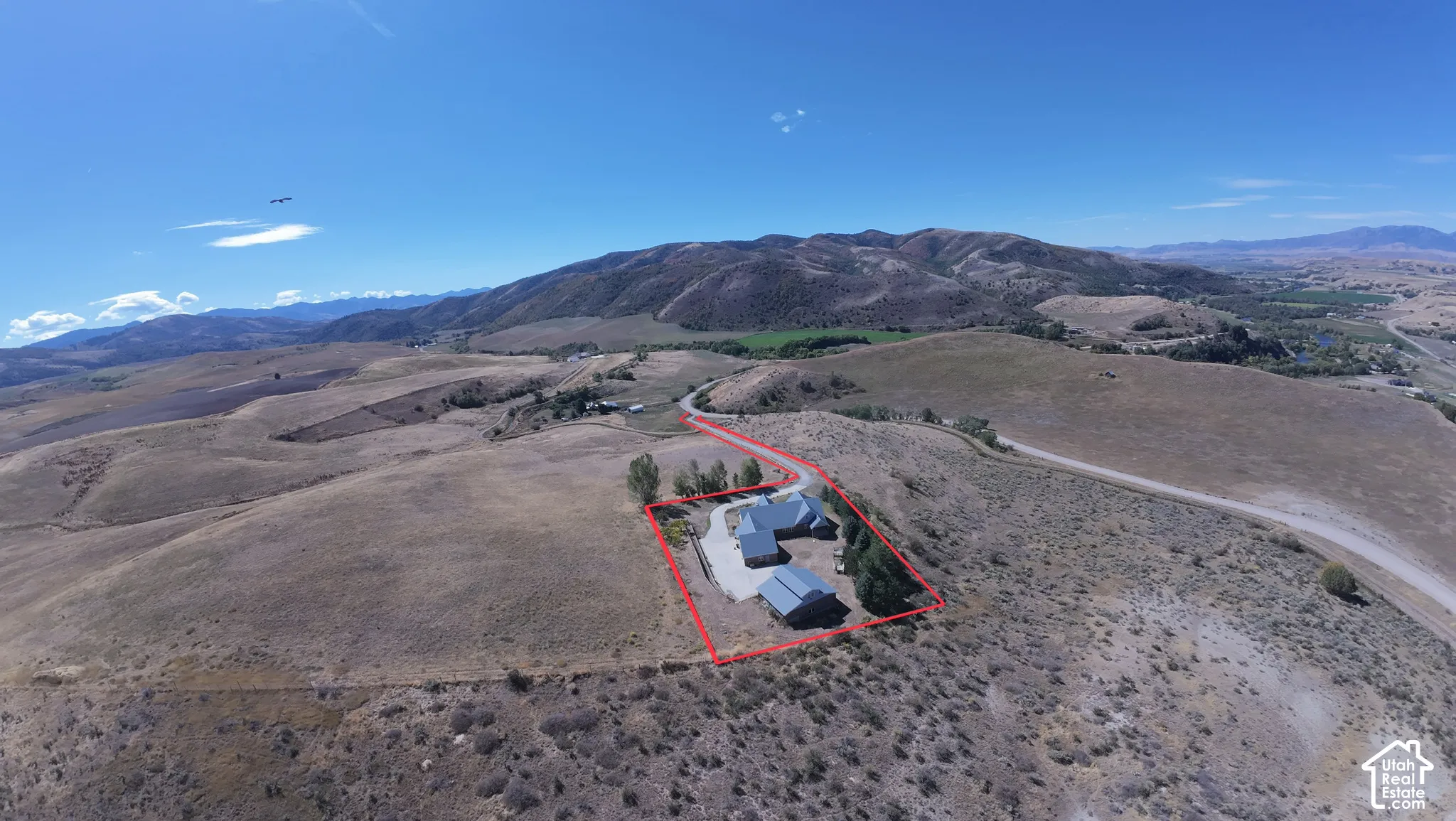 Aerial perspective of property featuring a multi-structure residence, paved driveway, mature trees, and expansive topography