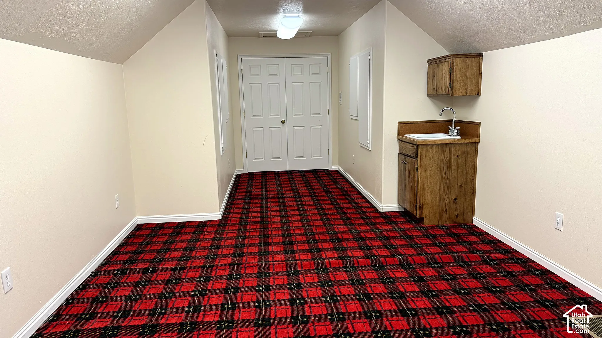 Finished space featuring vaulted ceilings, double doors, and a built-in wooden cabinet unit with a sink and faucet