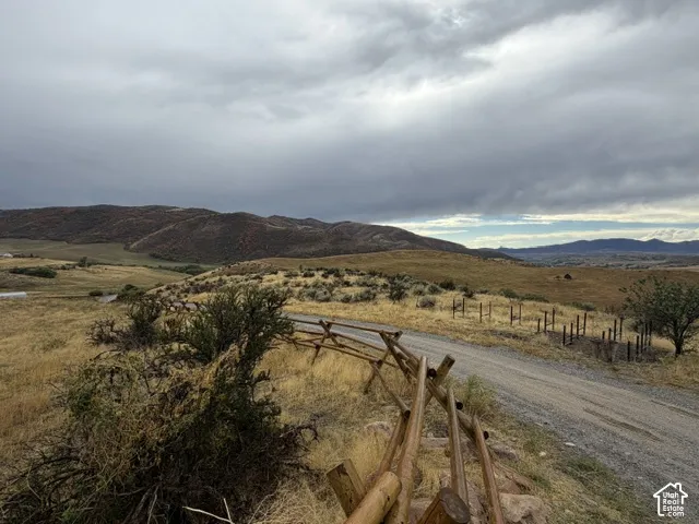 Gravel road with a rustic split-rail fence, surrounded by expansive natural terrain and distant hills