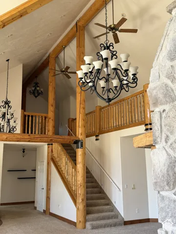 Vaulted ceiling with exposed wood beams, carpeted flooring, and a stone-clad fireplace