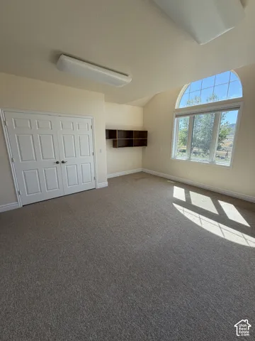 Arched window with exterior scenery, built-in shelving, vaulted ceiling, neutral carpet, and double bi-fold doors