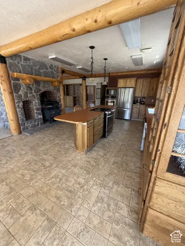 Tiled flooring, exposed wood beams, stone fireplace, wood cabinetry, and stainless steel appliances