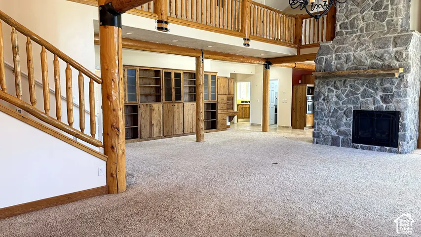 Vaulted ceilings with exposed log beams, floor-to-ceiling stone fireplace, built-in wooden cabinetry, and a mezzanine featuring a log-style railing